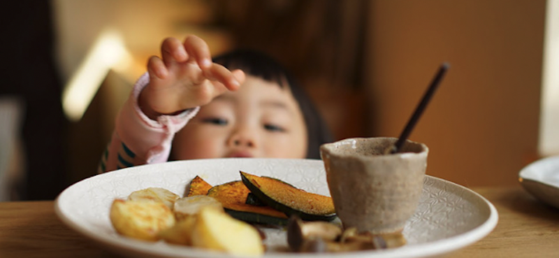 小さな子どもがテーブルの上の野菜に手を伸ばしている写真